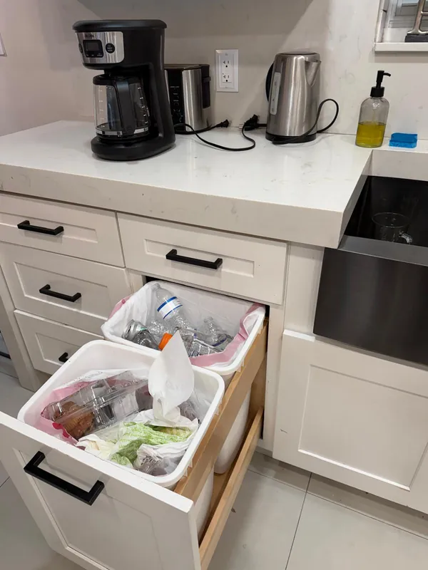 Kitchen trash drawer full of bottles and waste before cleaning
